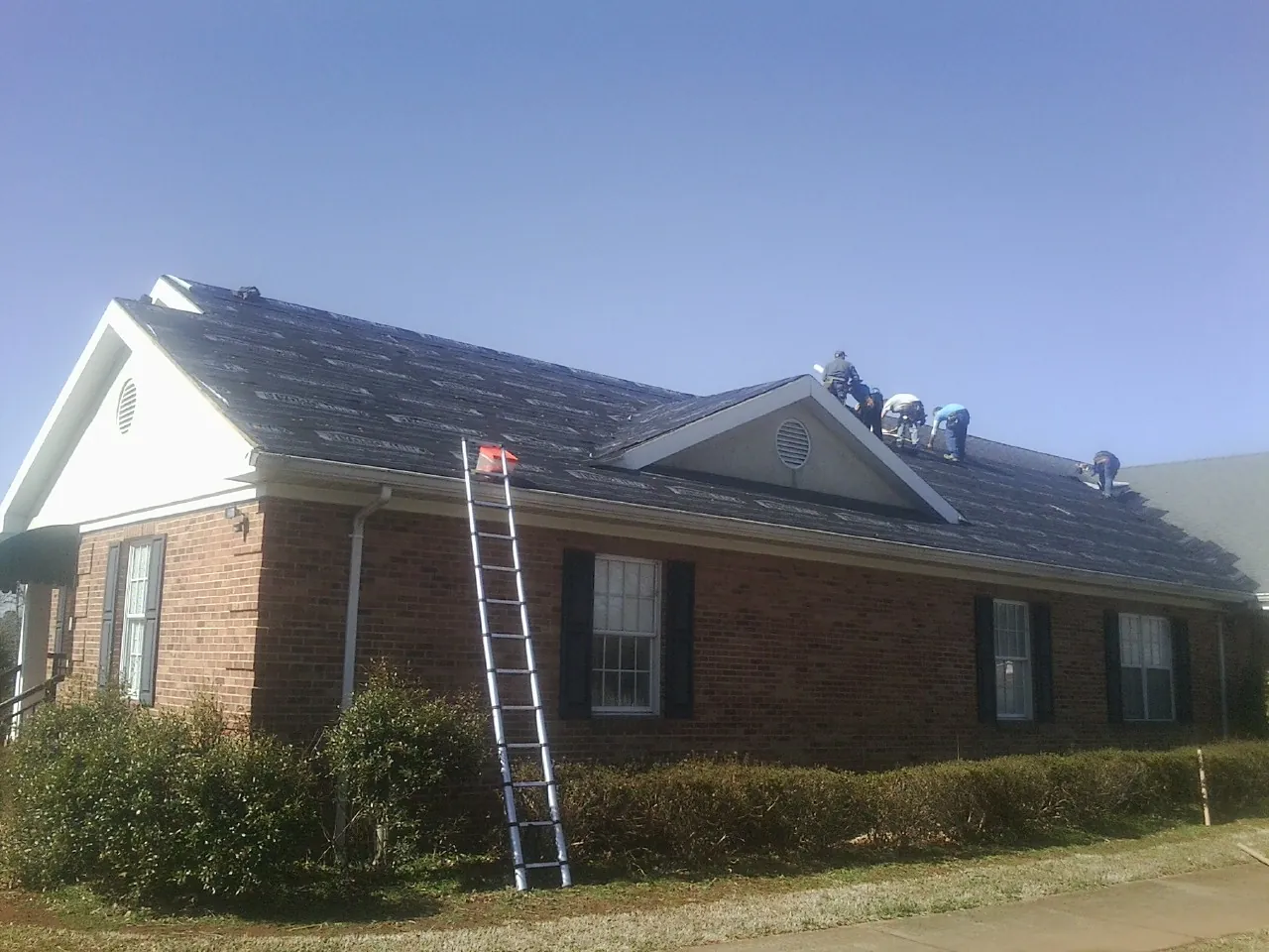 Crew tearing shingles off a brick ranch roof with a ladder set — Metal Roof Repair work by our crew in New Oxford