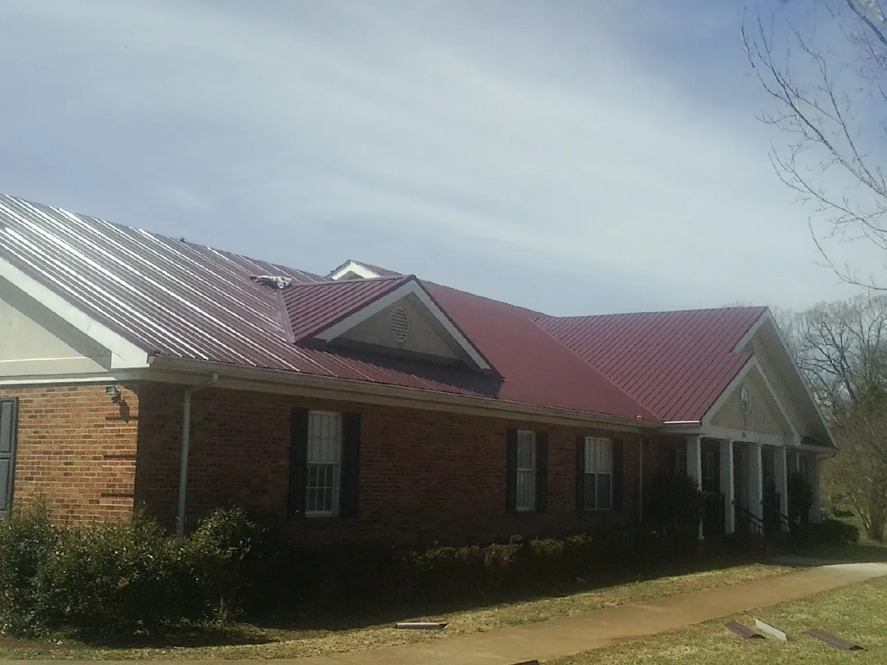 Red metal roof with gabled entries on a long brick building, from a Hail Damage Roof Repair job in New Oxford