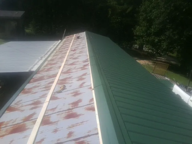 Old rusted panels beside newly installed green metal roofing — Wind Damage Roof Repair by Roofing Brothers in New Oxford
