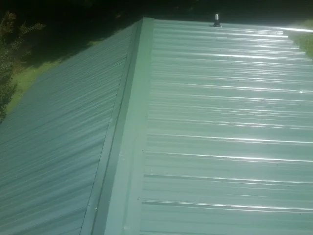 New green metal panels meeting at the ridge of a roof — Flat Roof Repair work by our crew in New Oxford