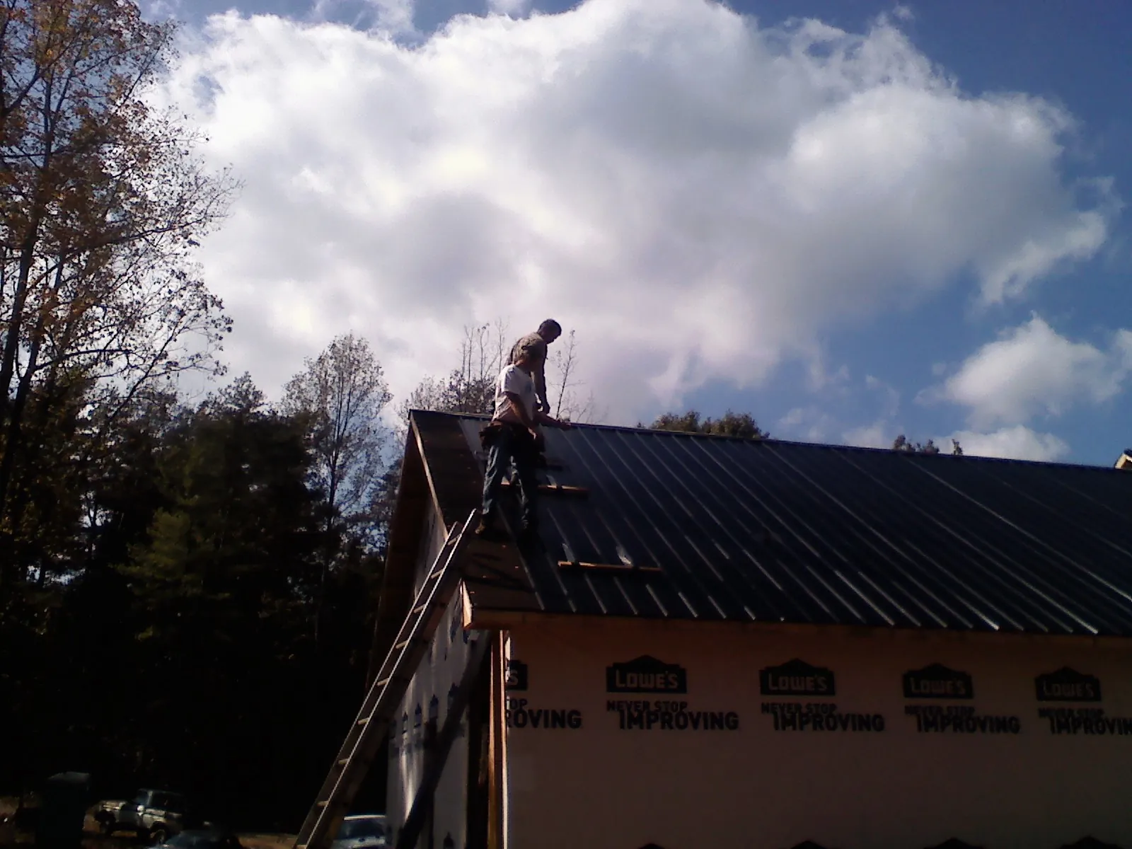 Roofer fastening dark metal panels high against a cloudy sky, from a Roof Inspection job in New Oxford