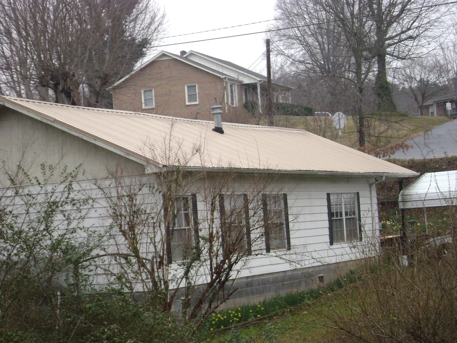Tan metal roof on a white sided house set into a hillside — Commercial Roofing by Roofing Brothers in New Oxford